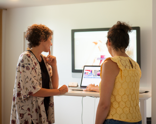 Deux femmes debout devant un bureau regardent un ordinateur 